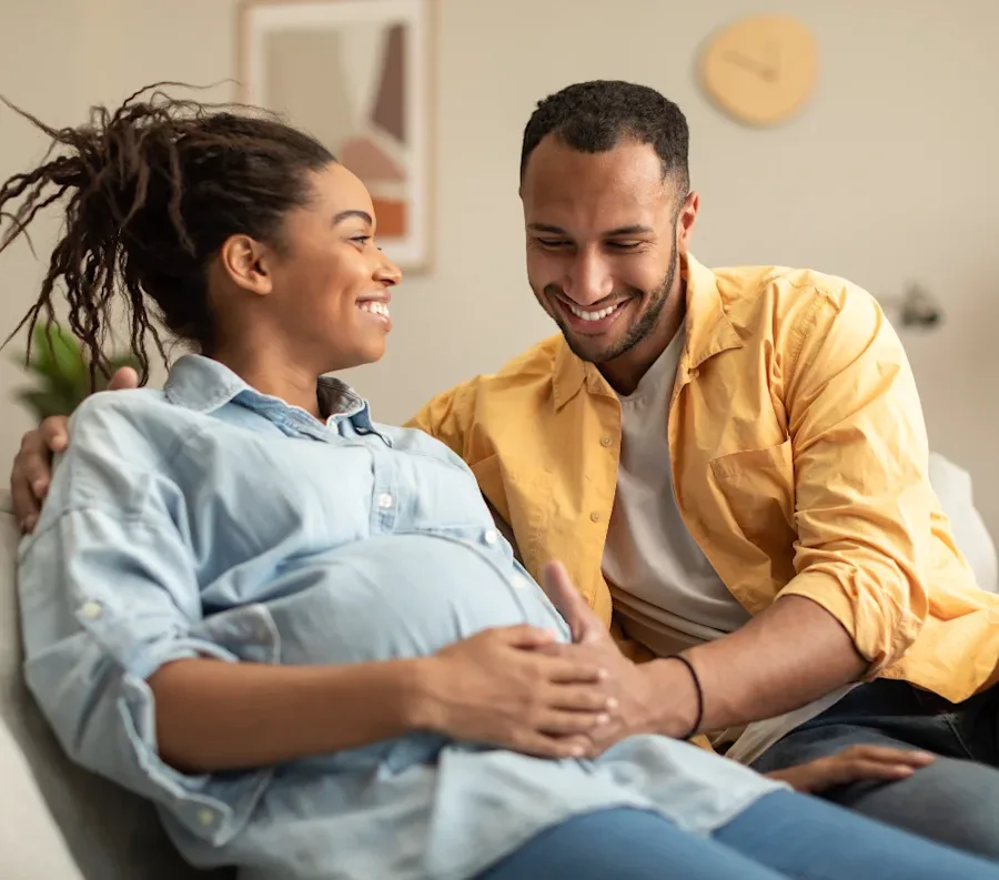 A couple seated on a couch smiling.
