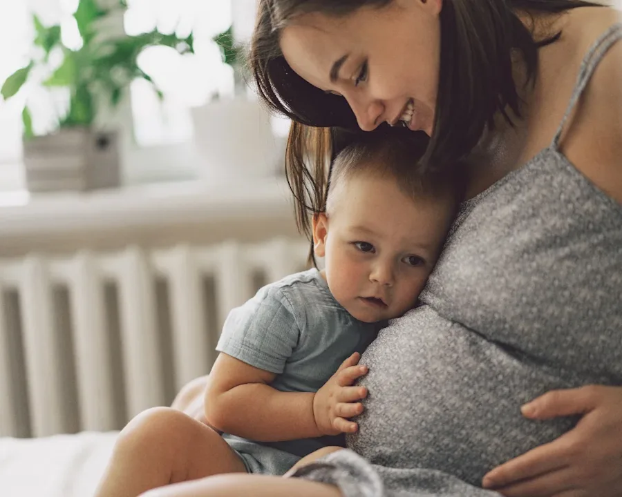 A pregnant person smiling with their child.