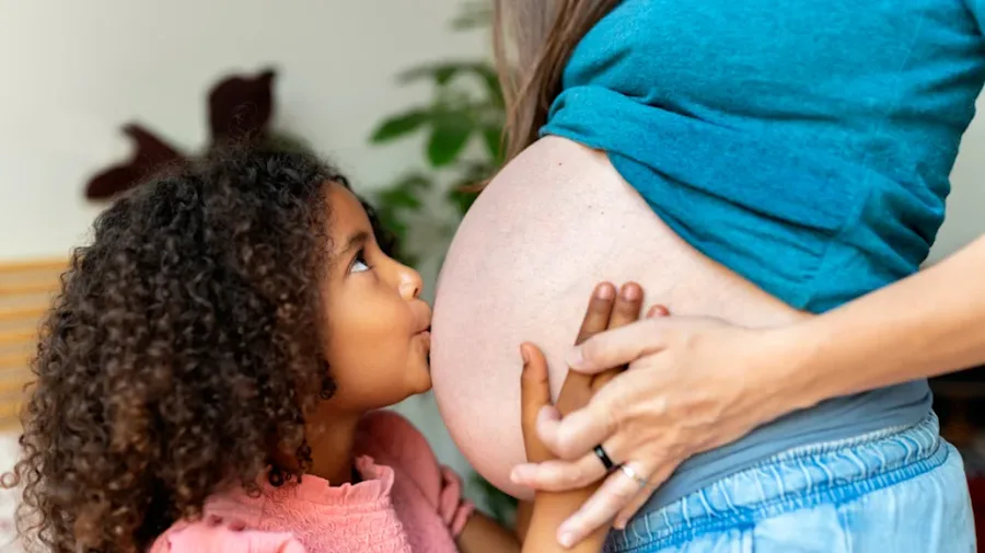 A child kissing a belly of her pregnant mother.