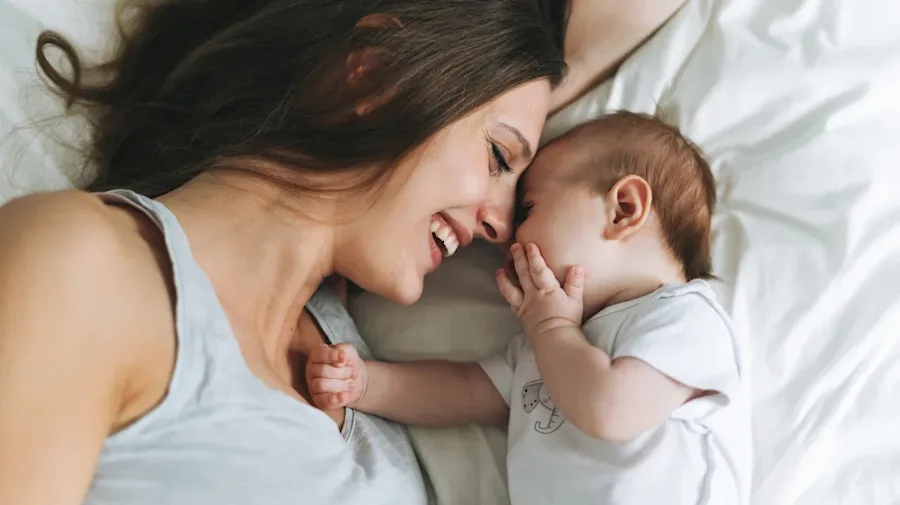 A parent laying down next to a baby smiling.