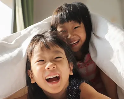Two children laughing under a blanket.