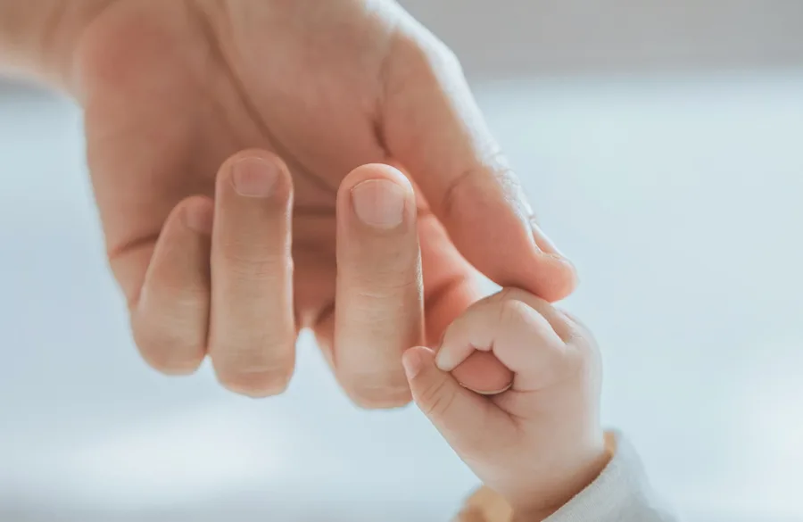An infant hand holding the fingers of an adult.