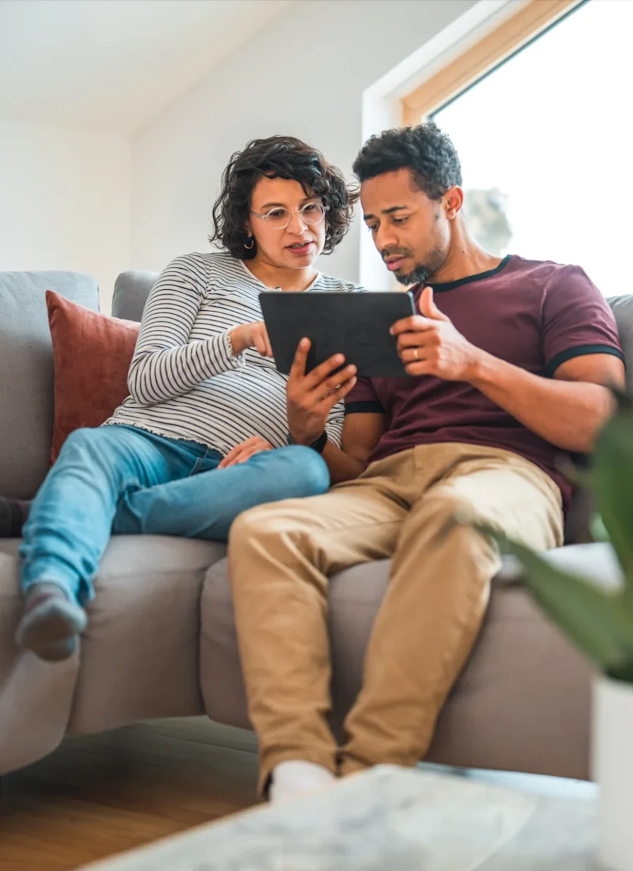 A couple seated on a couch, interacting with a tablet.