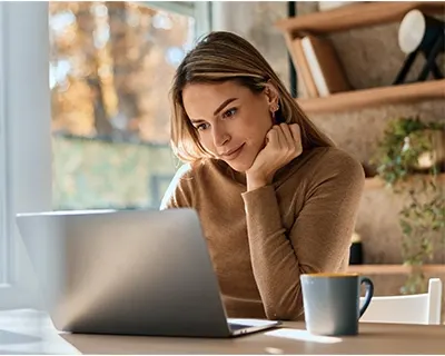 Woman working on her computer while drinking coffee.