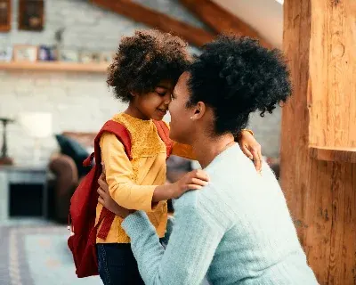 A parent embracing their child with a backpack, smiling.