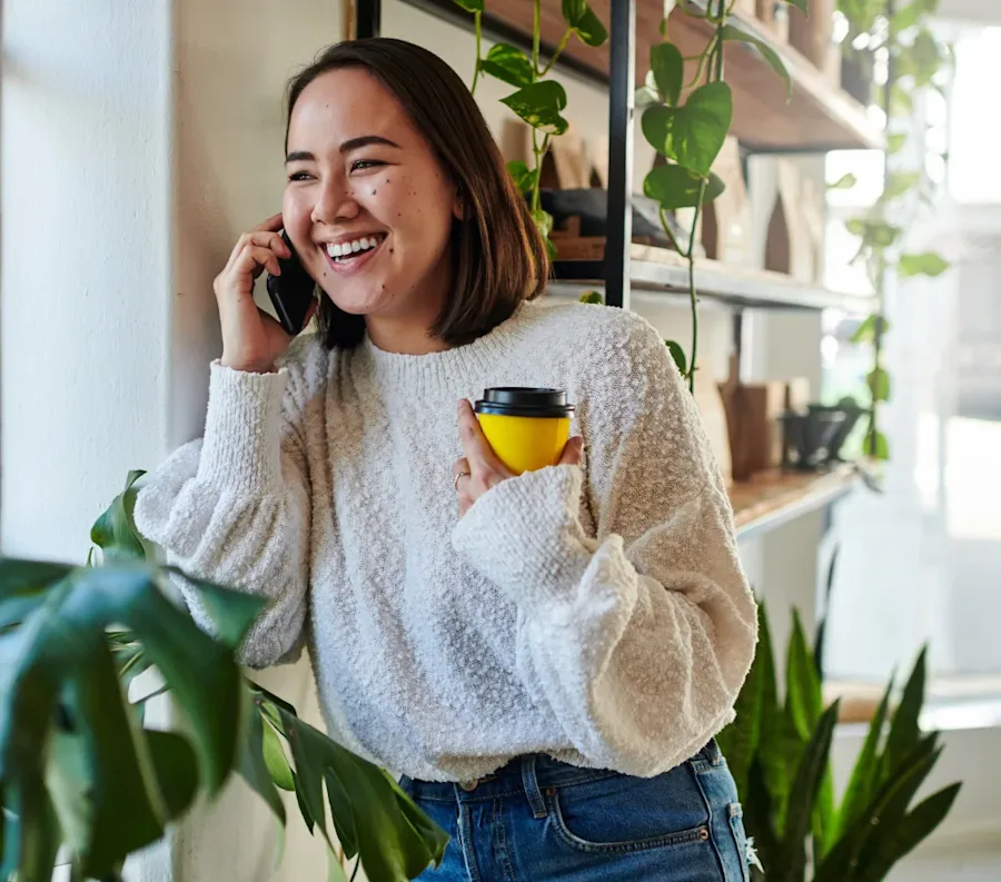 A person holding a coffee, smiling while speaking on the phone.