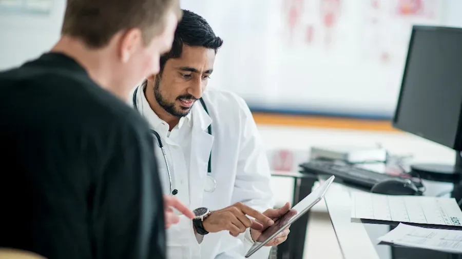 A medical professional discussing information on a tablet with another person.  