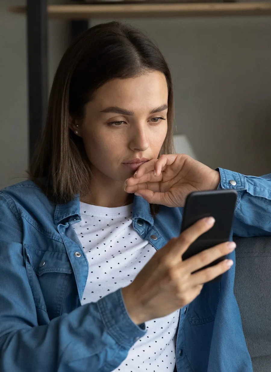 A woman holding her cell phone and touching her face.