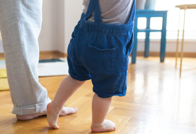 Legs shown of a baby and parent walking.