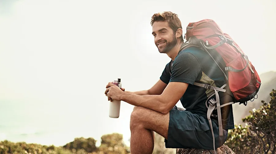 A person wearing a backpack on a hike, smiling.