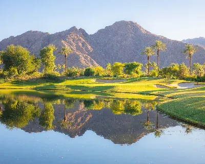 A view of green grass, trees, and mountains behind water.