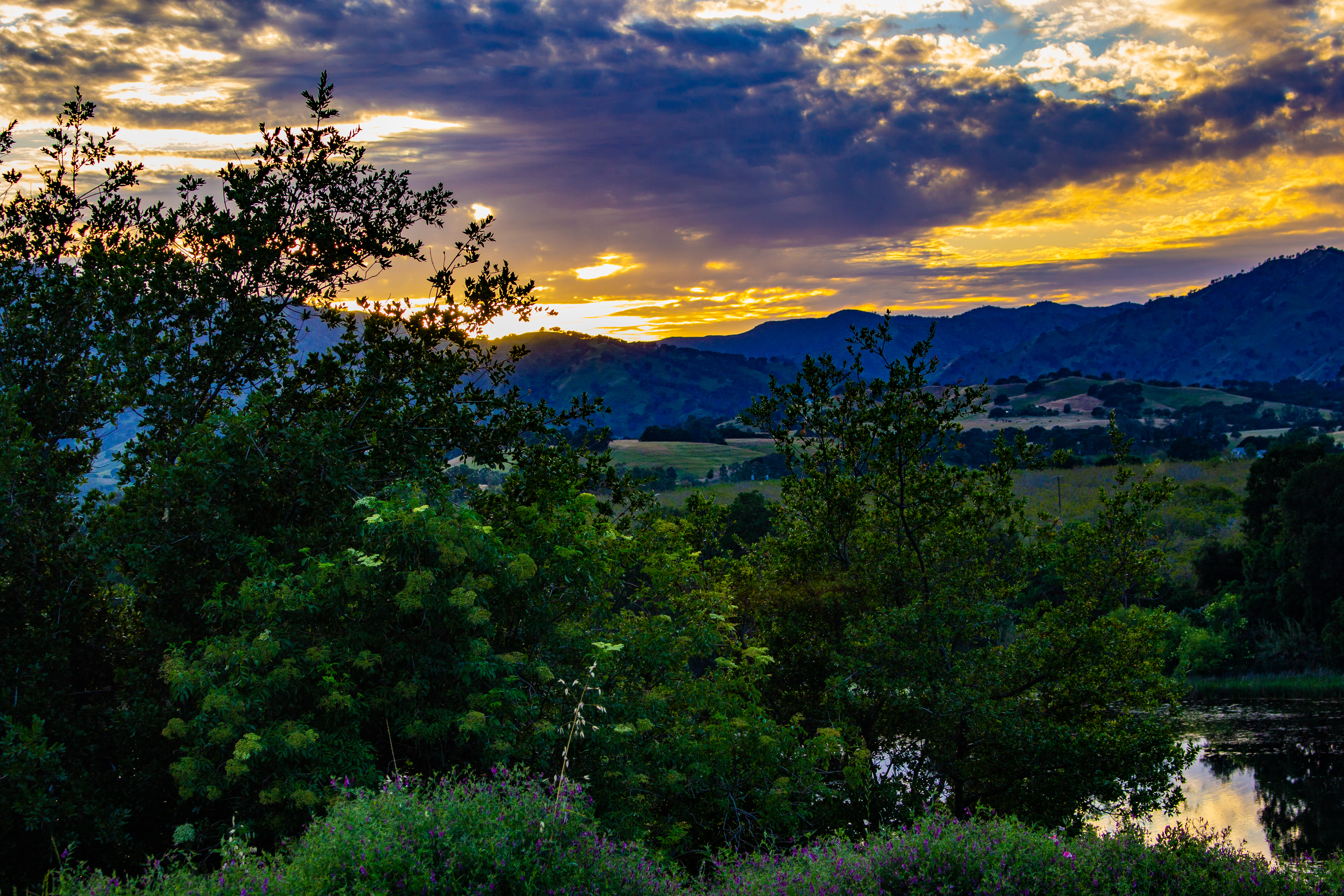 A photograph of the sunset, above a mountain, beyond a river.