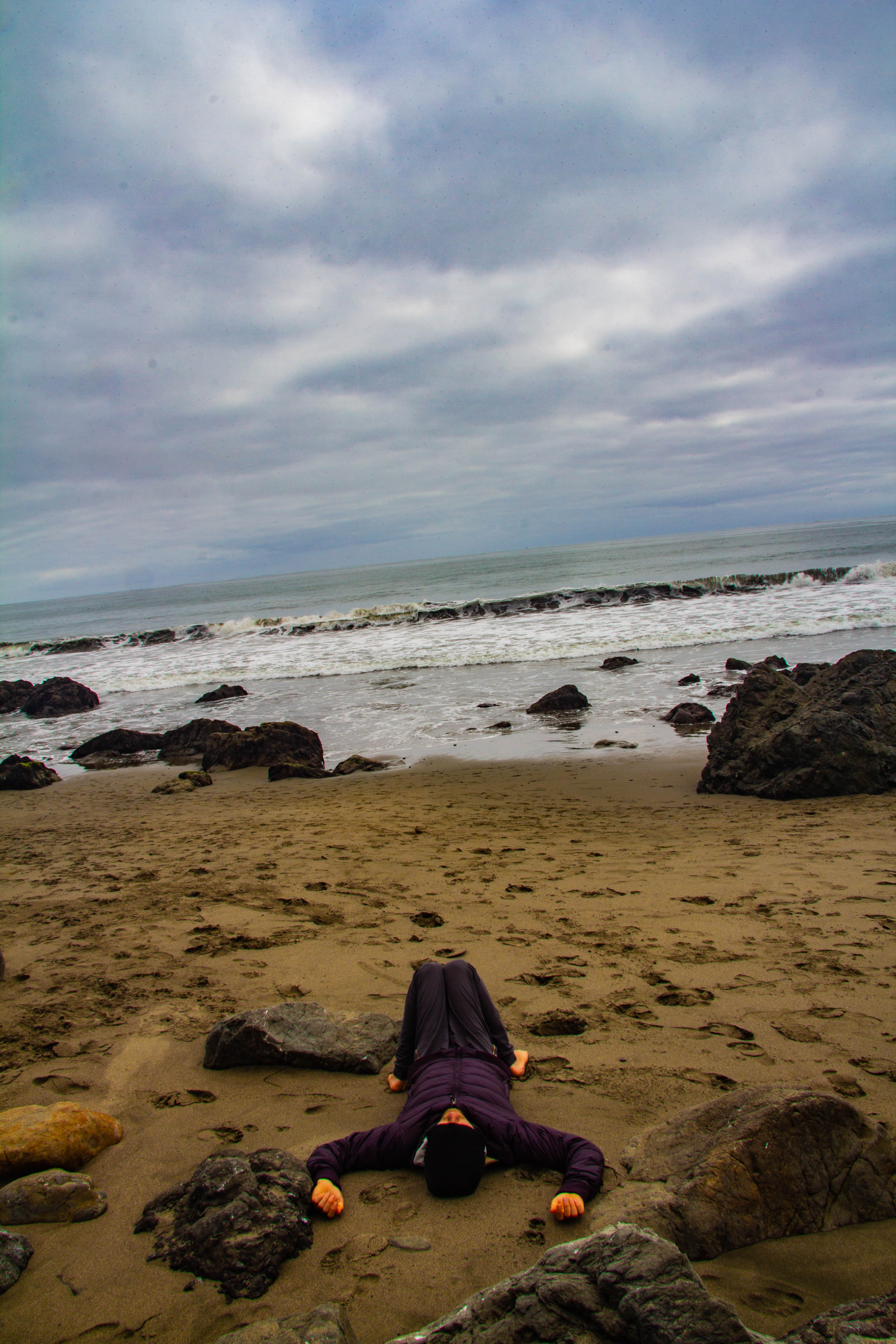 A photograph of a person laying on a beach on an overcast day.