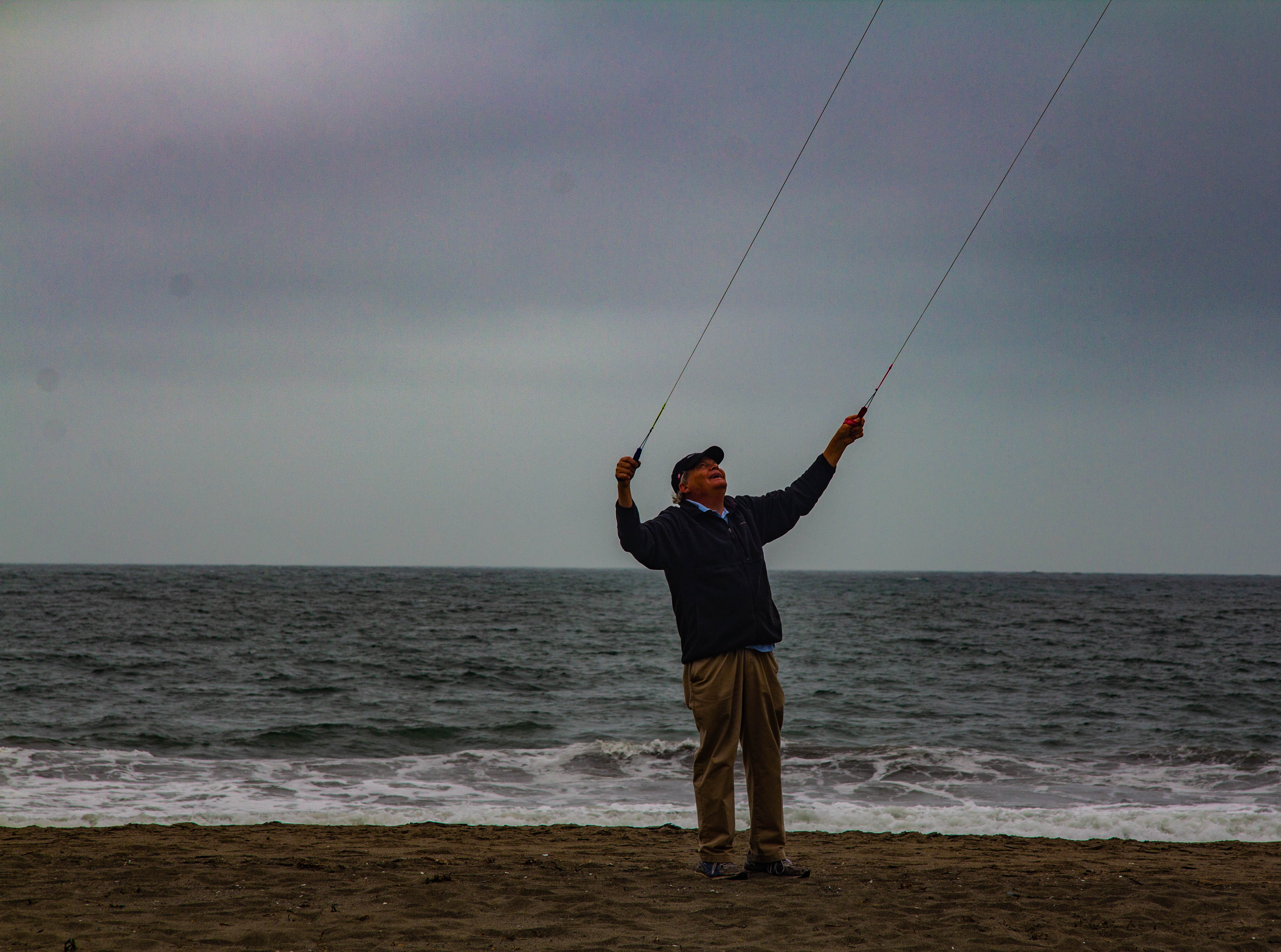 A photograph of a man flying a kite on a beach.