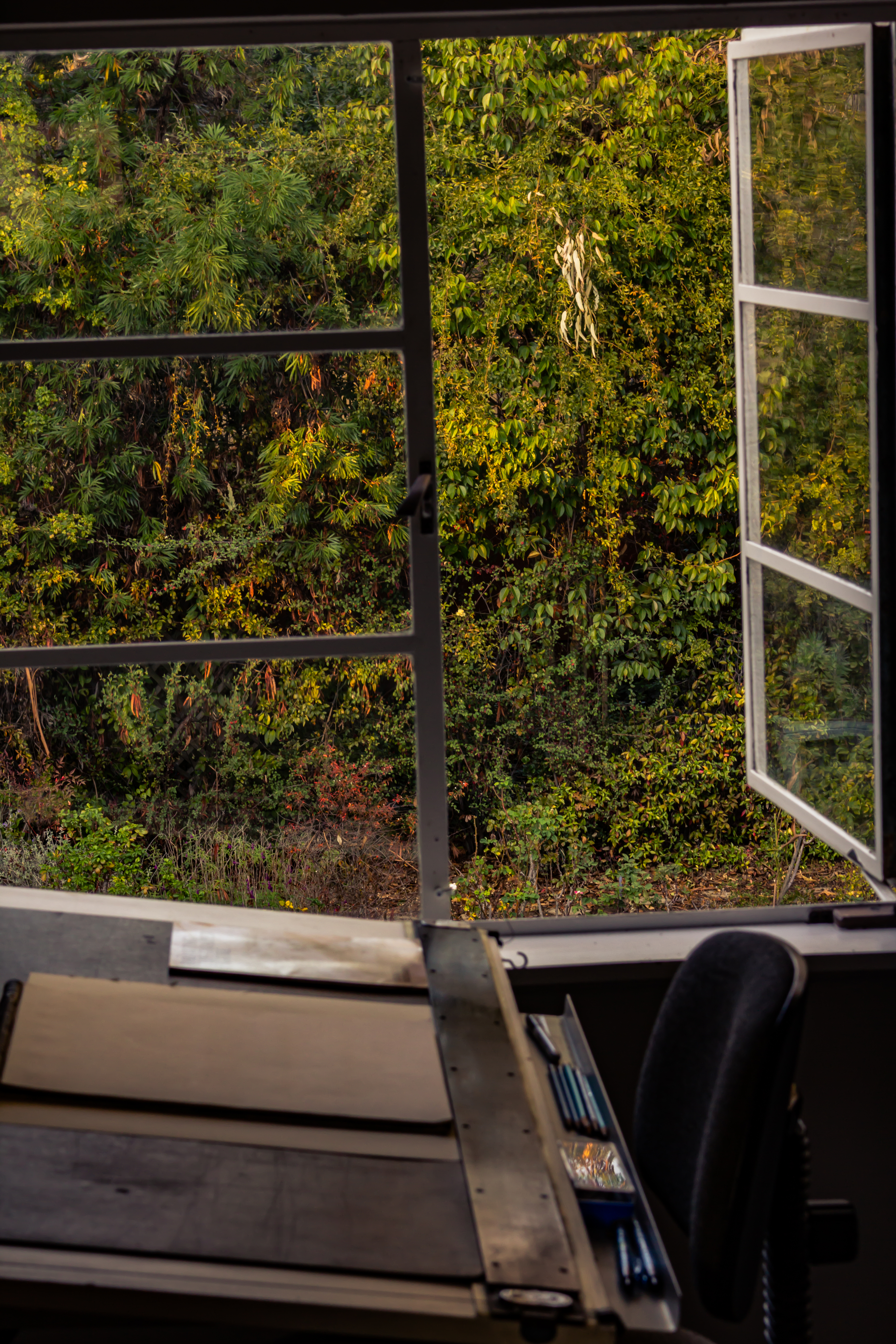 A photograph of a drafting desk in front of an open window.