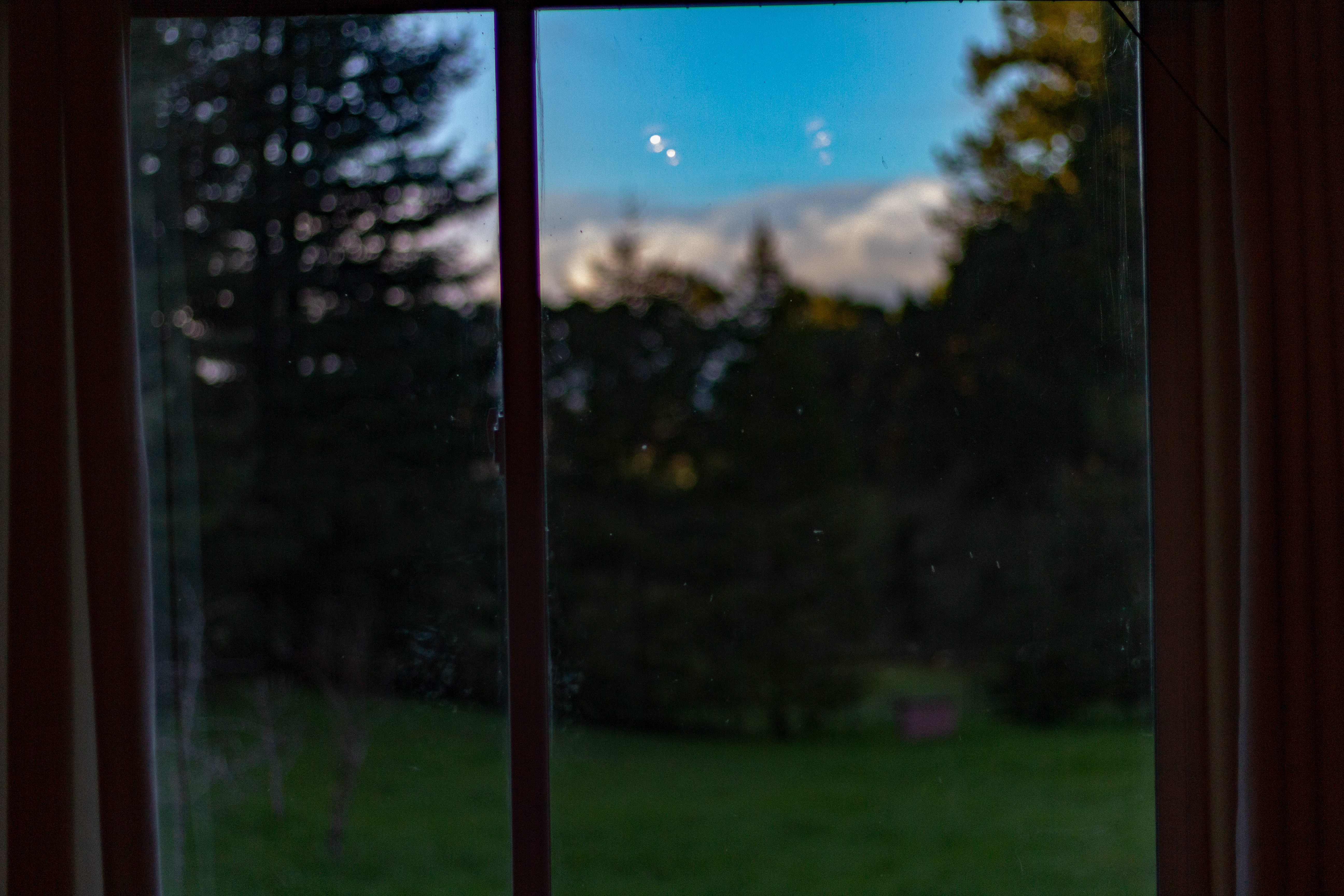 A photograph of a window, showing a bright blue sky and green field beyond.