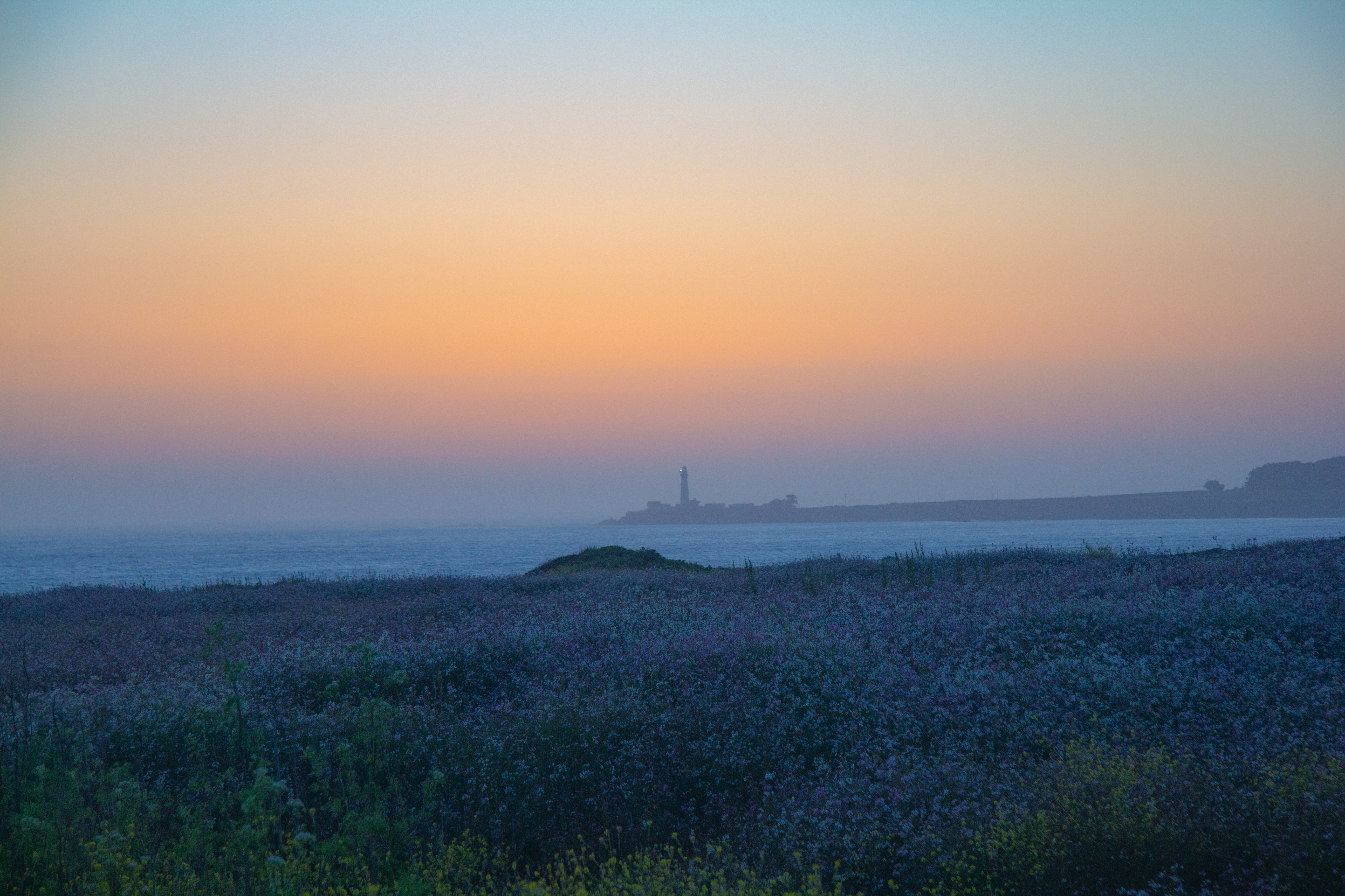 A photograph of a lighthouse in the distance, briefly after sunset.