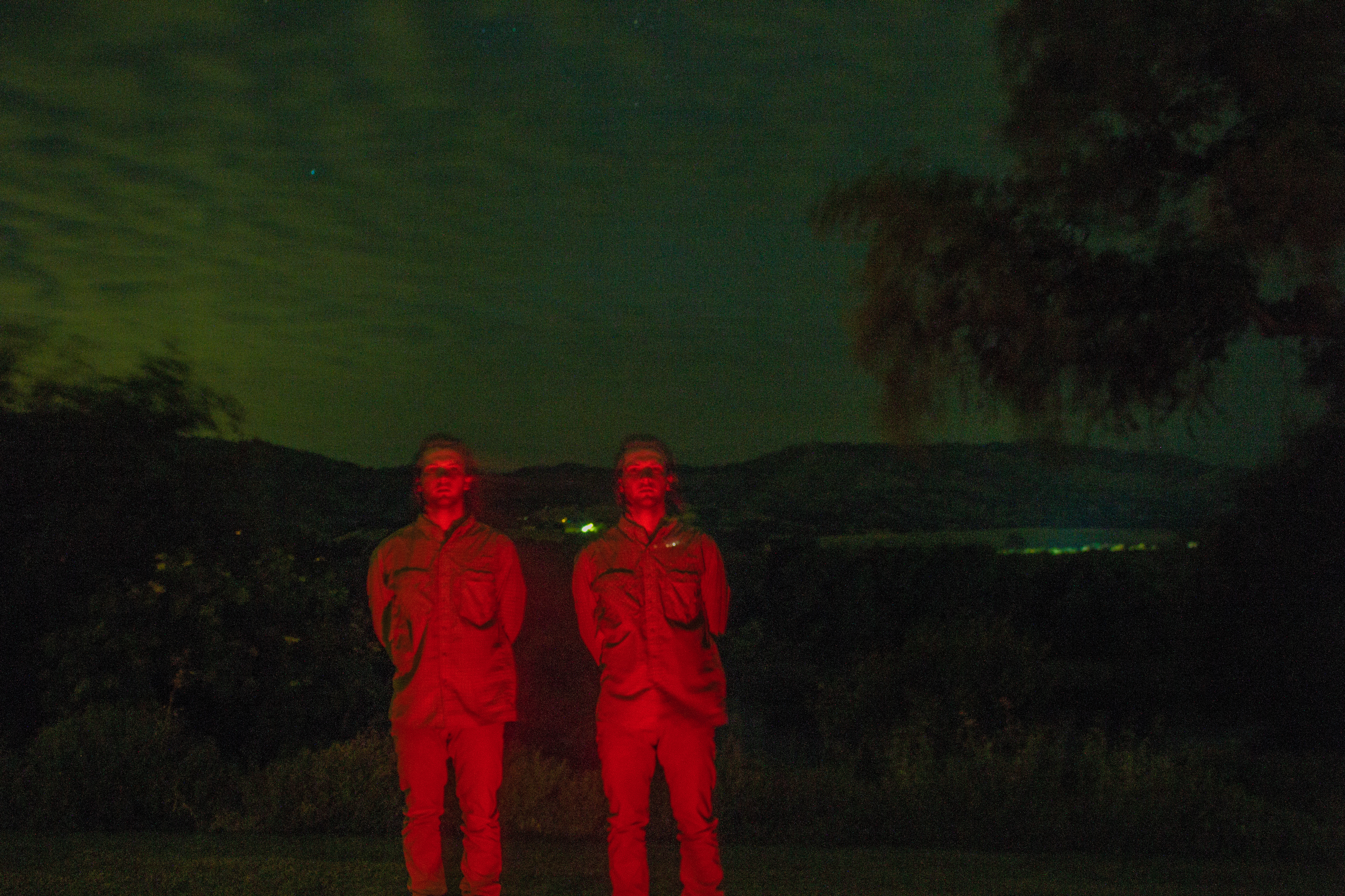 A photograph of two of the same person, glowing in the green night.