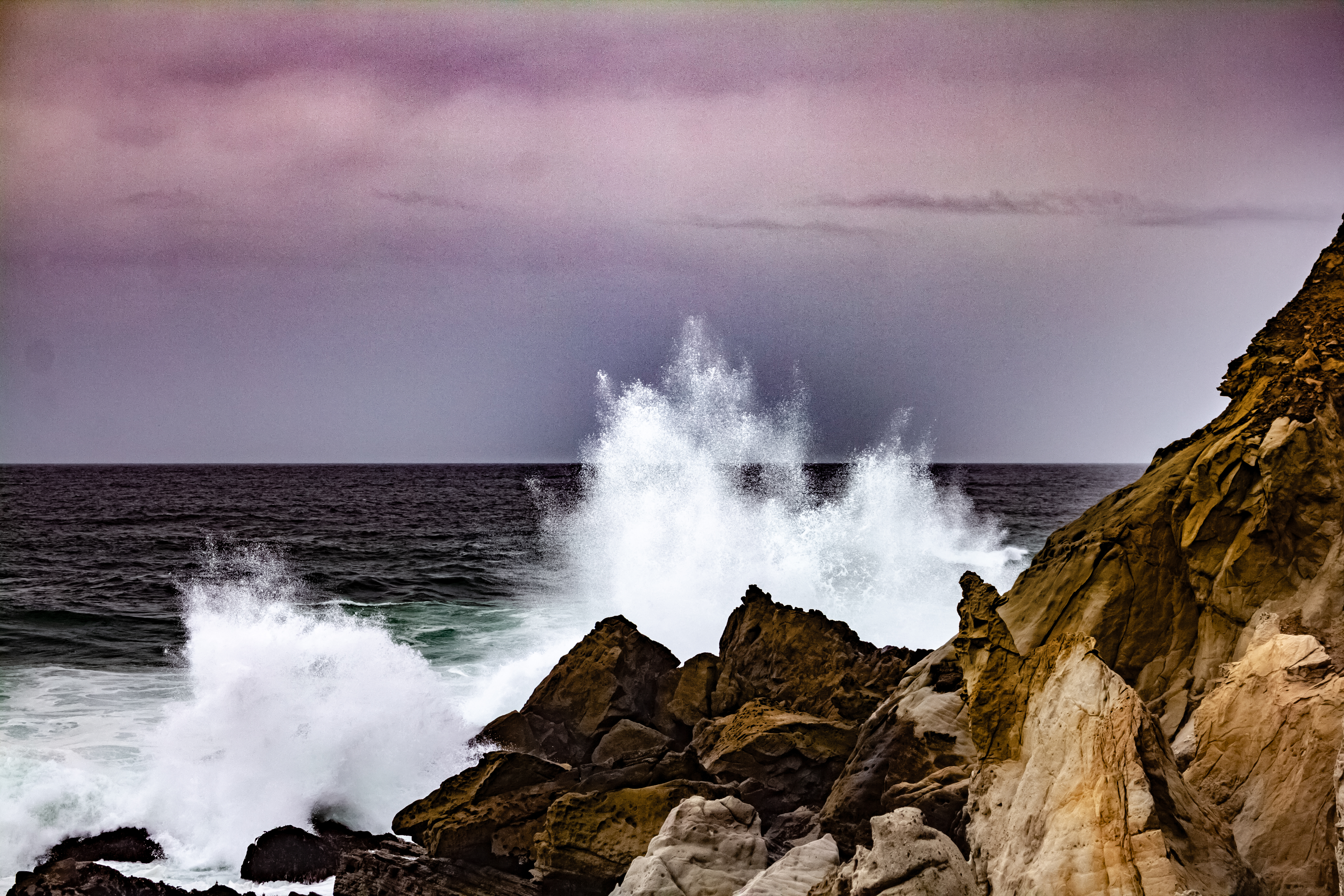 A photograph of the ocean spray coming off a rock as a wave hits it.