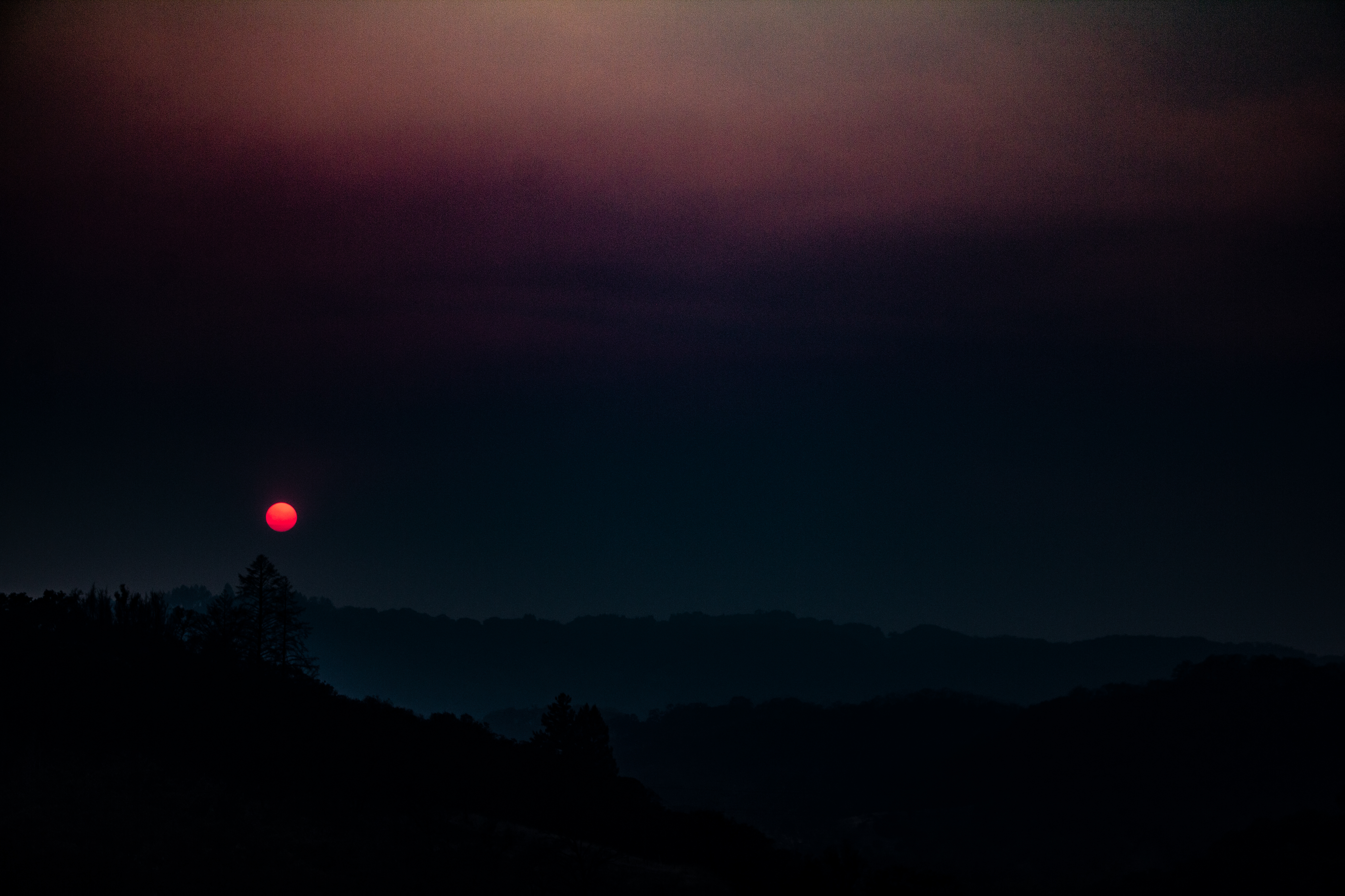 A photograph of a red sun as it sets behind the mountains.