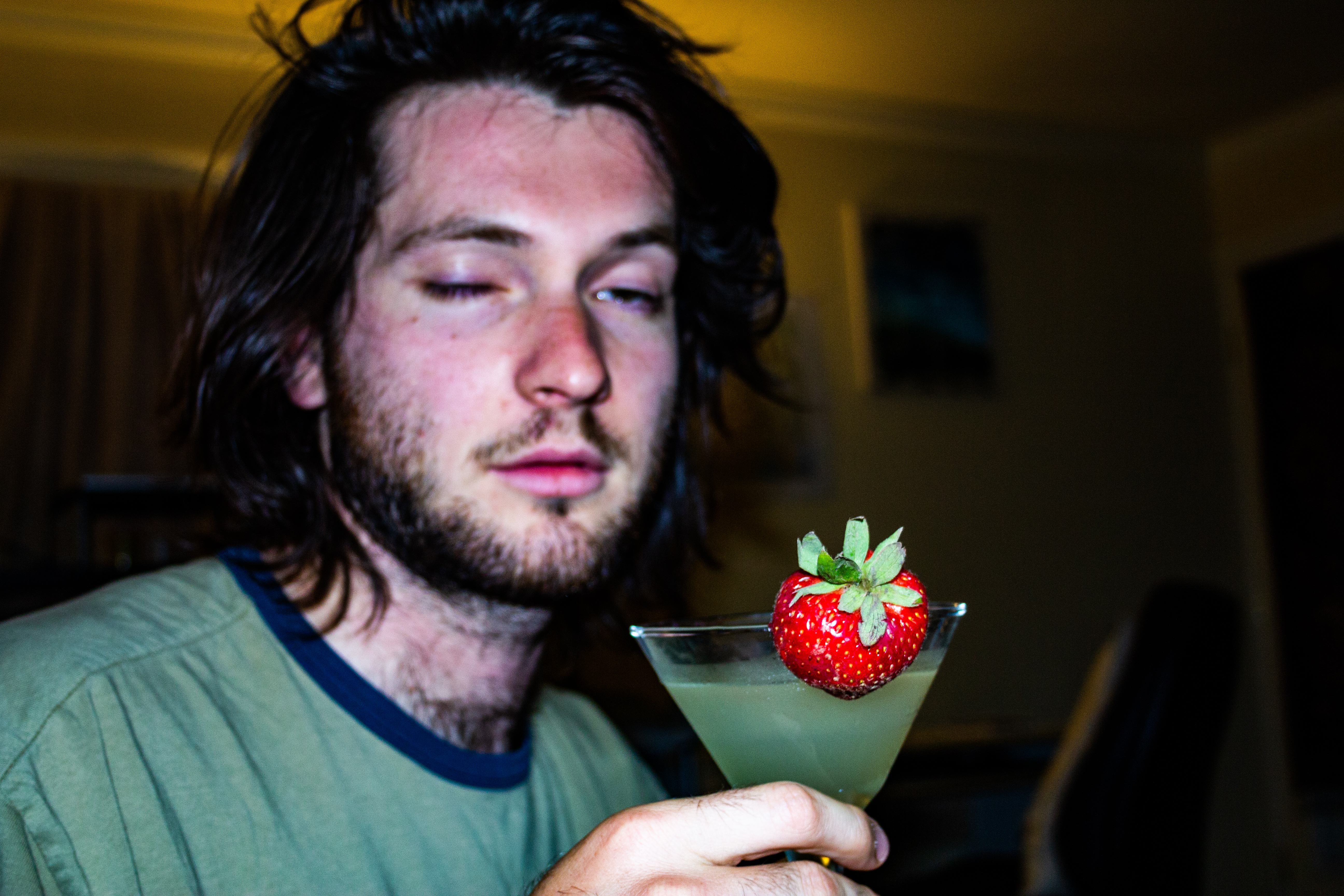 A photograph of a strawberry on the rim of a full glass, held by a person.