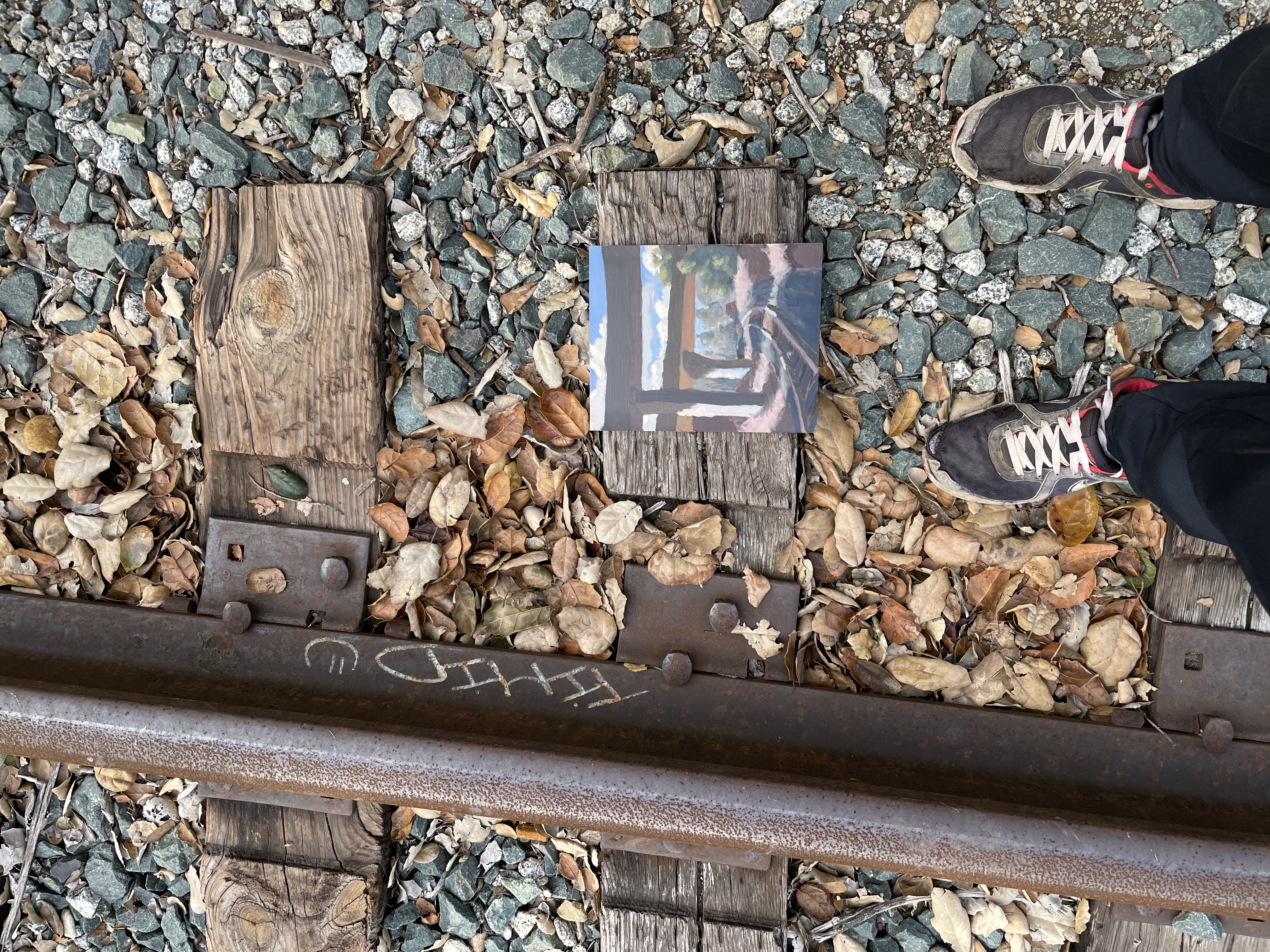 A photograph of a painting placed next to some railroad tracks.