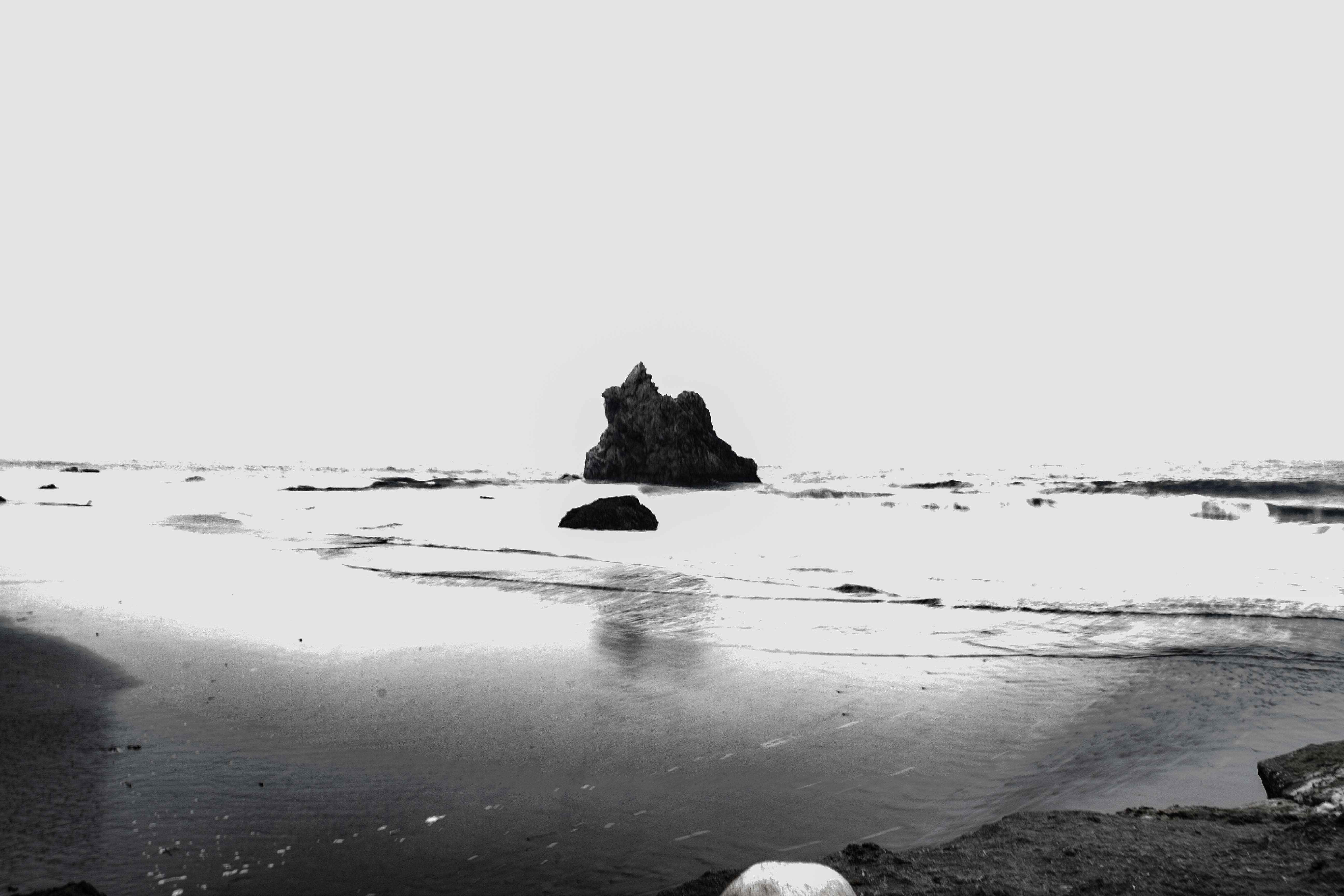 A photograph of a rock beyond the waves rolling into a beach.