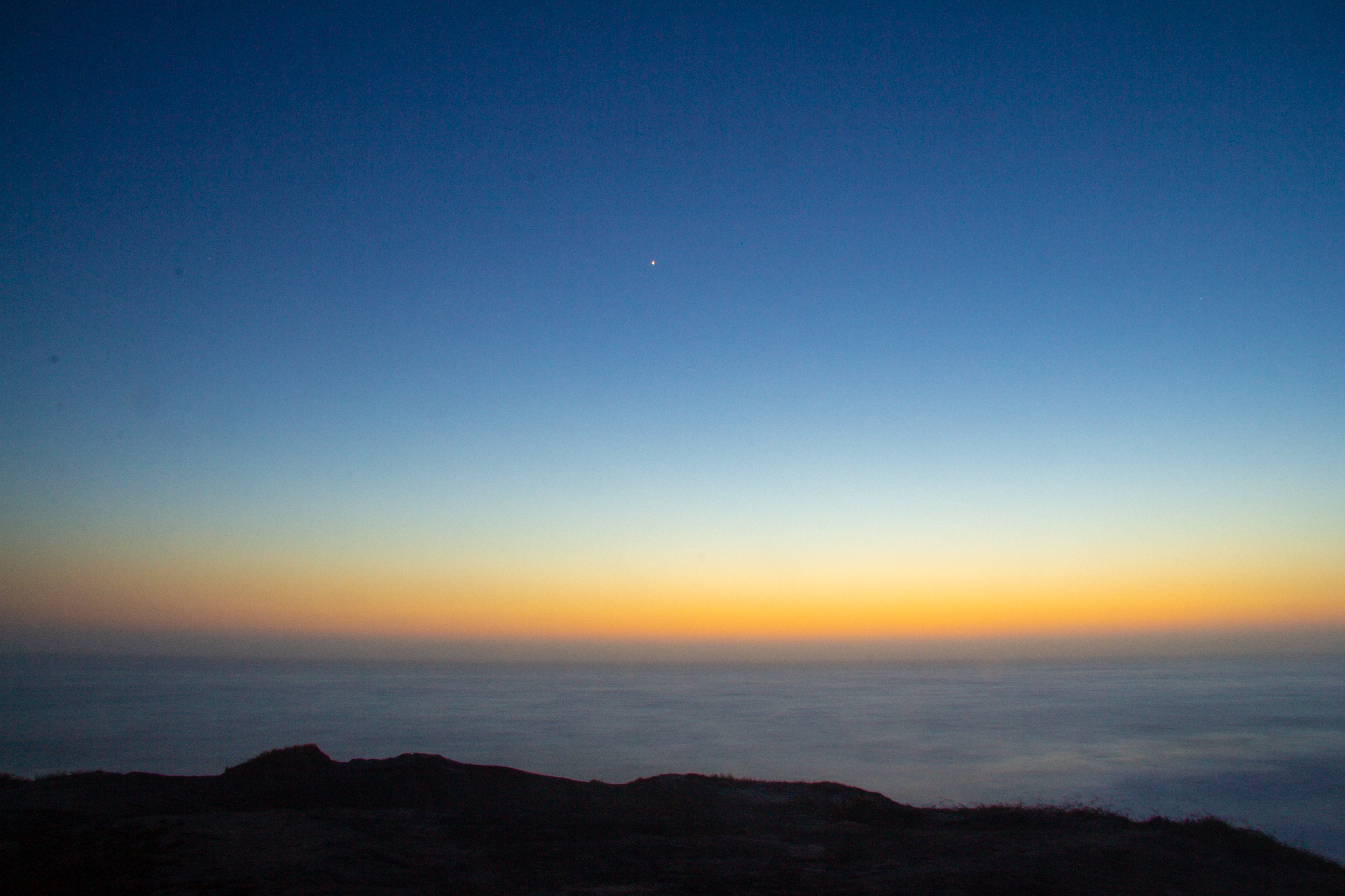 A photograph of a single star in the sky over the ocean just after sunset.