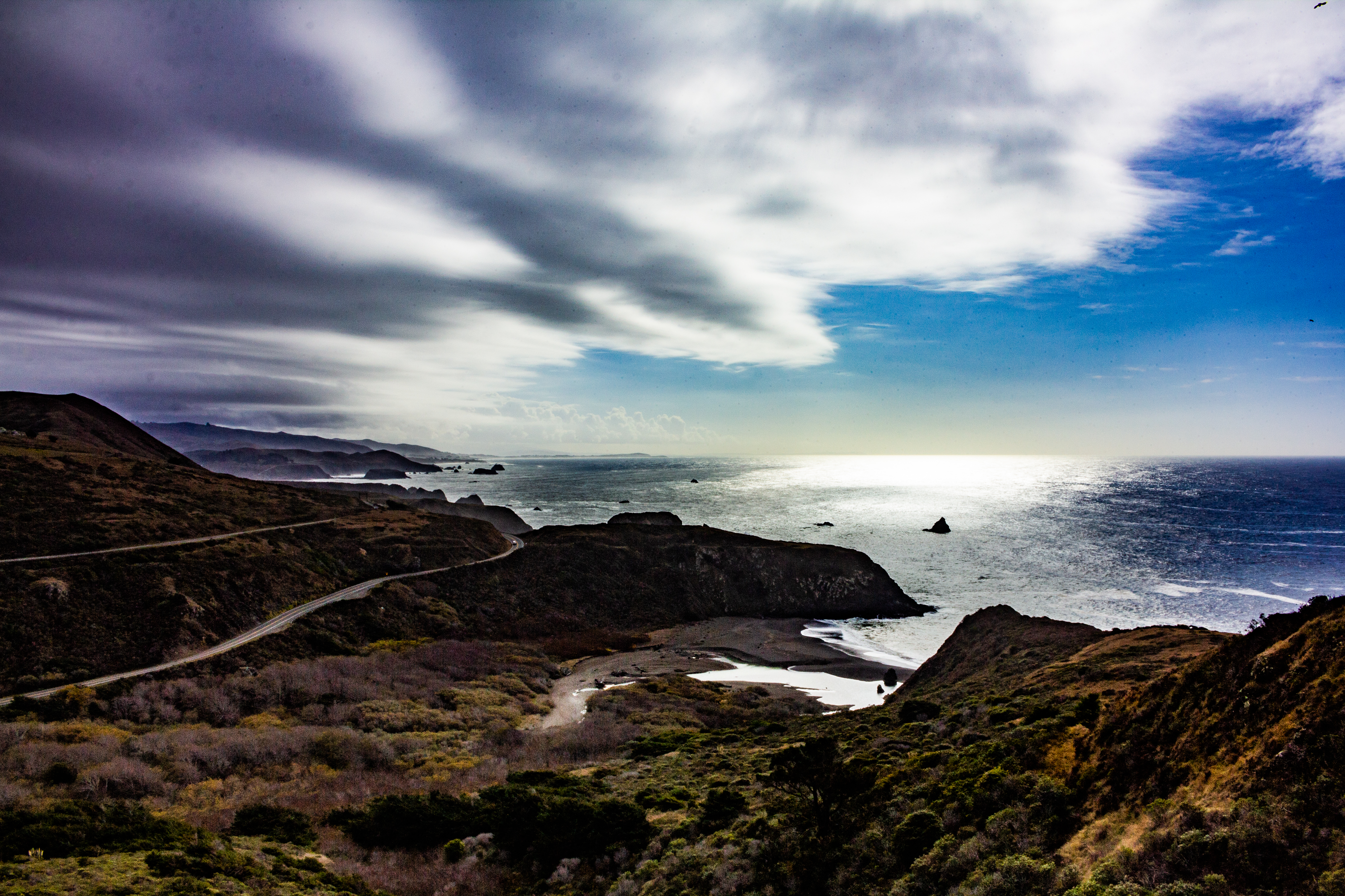 A photograph of the view from a high vantage, overlooking a road as it meanders along the ocean coast.
