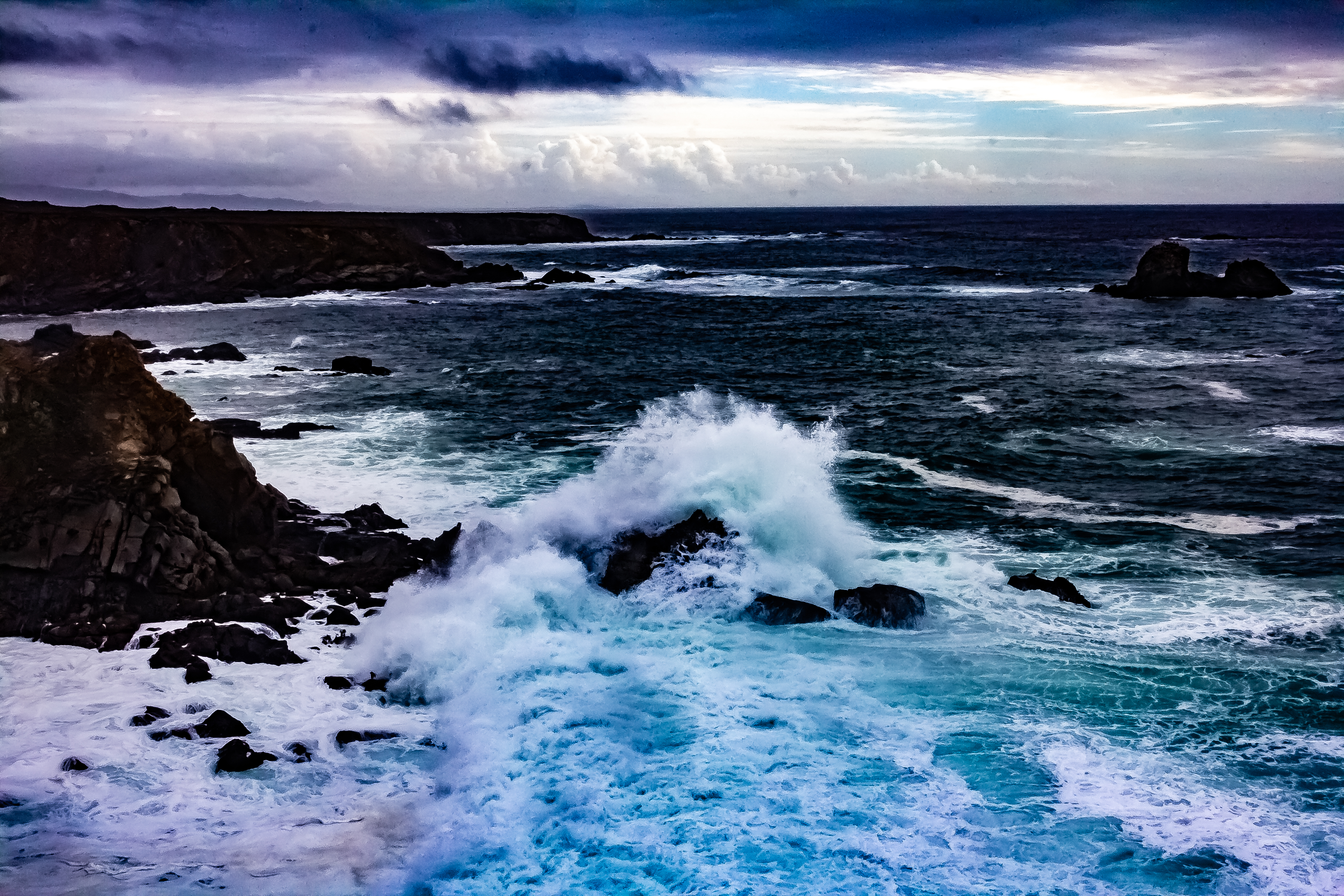 A photograph of a splash of ocean water as a wave hits a rock.