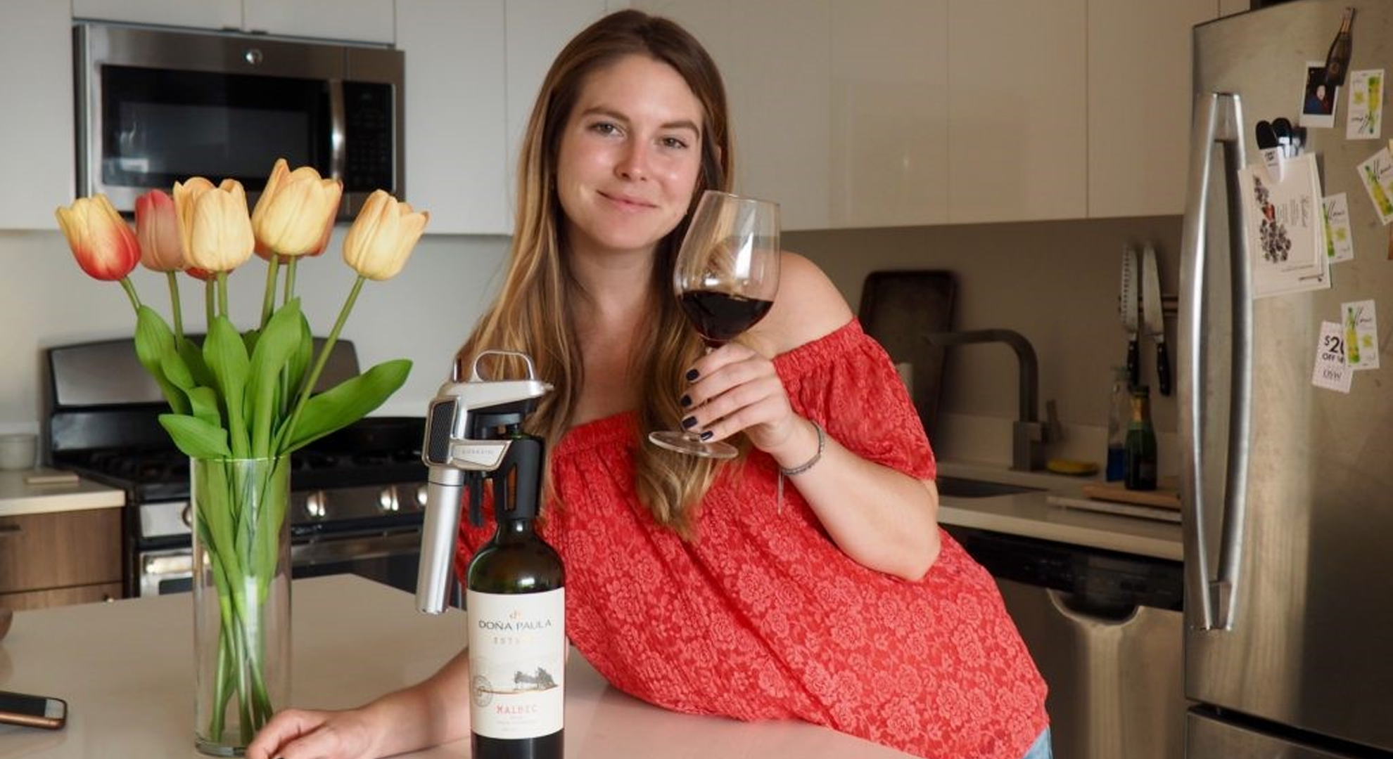 Chelsie Petras of Chel Loves Wine with a red wine glass and Coravin on a red wine bottle.