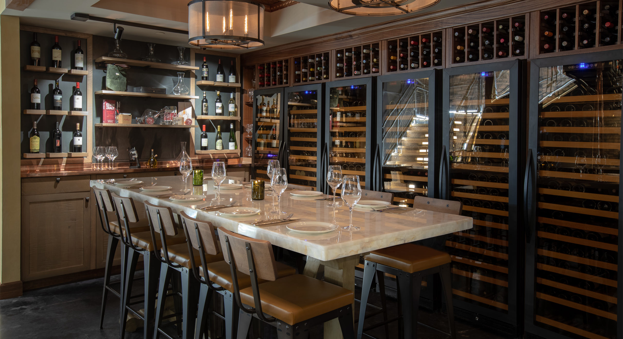 Elegant dining table setup with a background display of wine bottles, wine fridges, and wine cellar storage.
