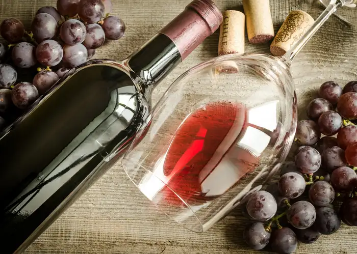 red wine in a glass next to a wine bottle and grapes.