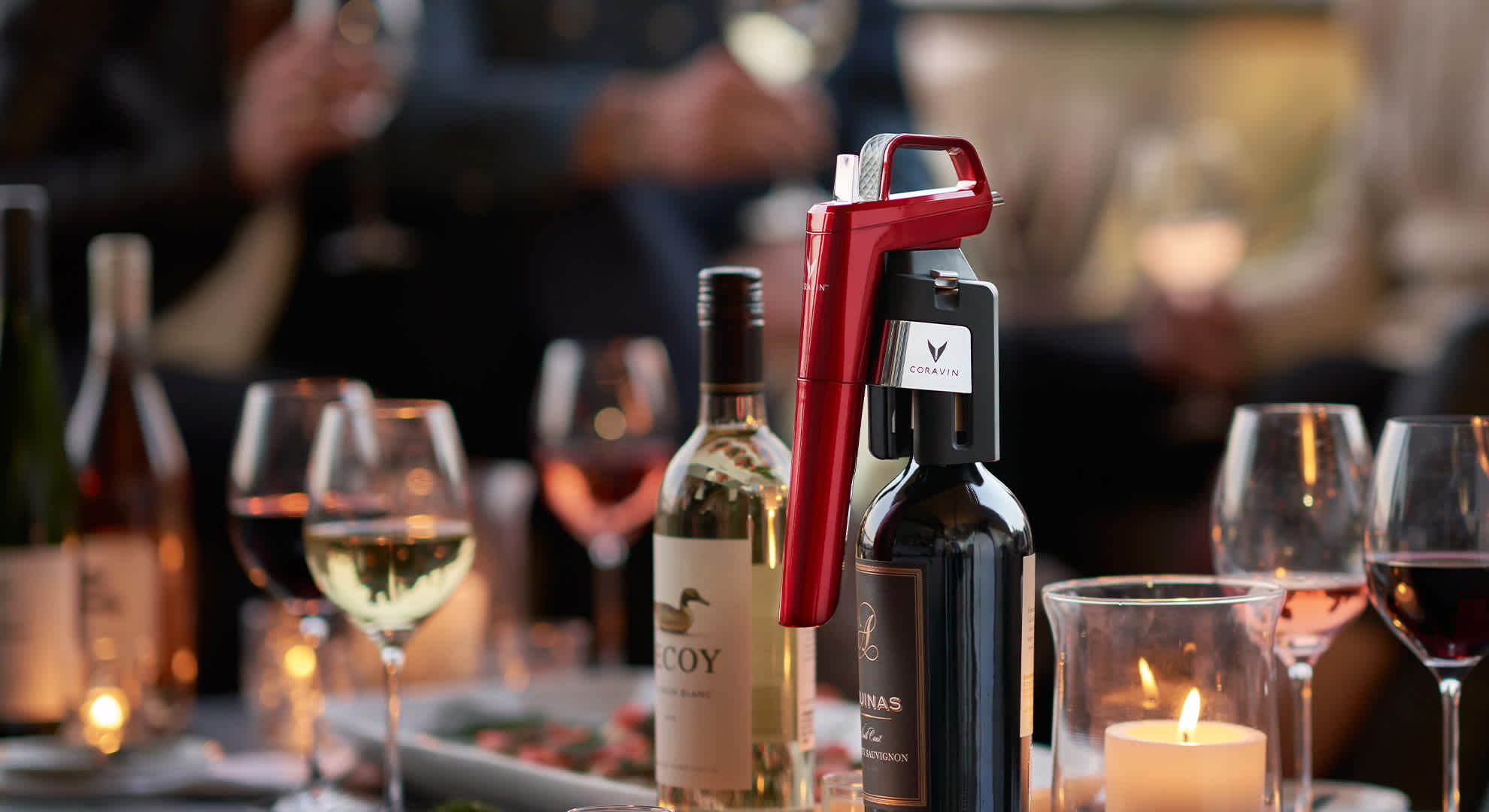 Model Six on bottle outdoors on a patio with wine glasses, candelight, and people in the background.