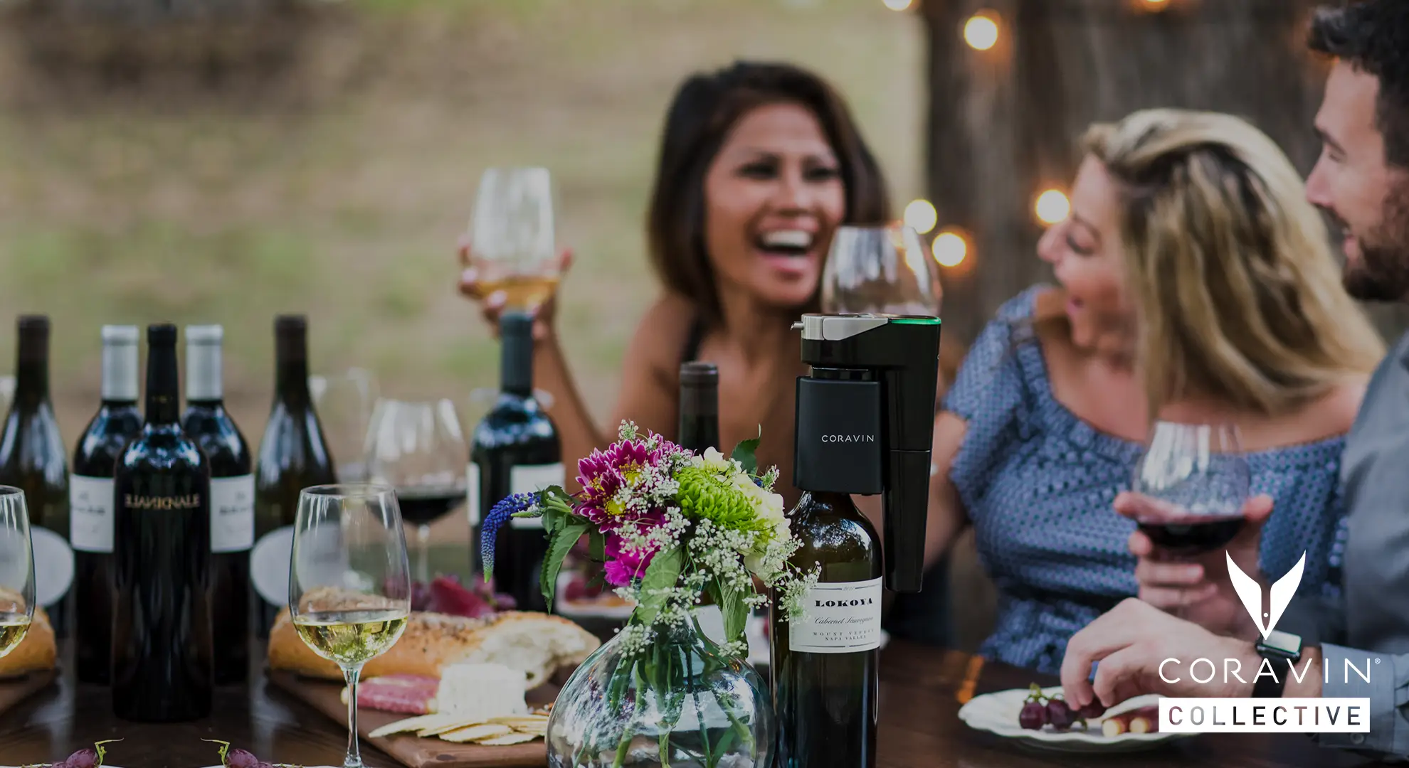 Friends using a Coravin to drink red and white wine outdoors at a picnic table, featuring the Coravin Collective logo. 