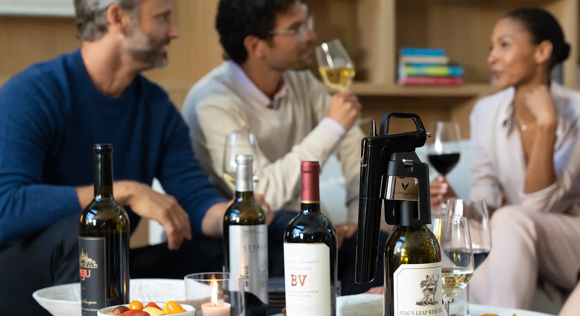 Eine Gruppe von Freunden in Wohnzimmer mit Wein und Fingerfood, im Vordergrund ein Coravin Weinsystem
