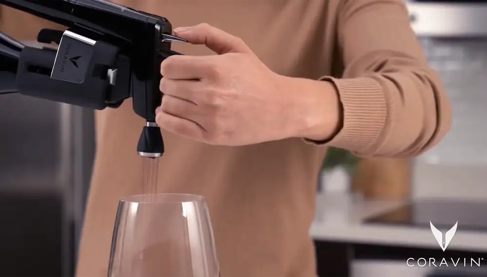 A close up of a woman pouring red wine into a glass using a Coravin Wine Preservation System and Coravin Aerator.