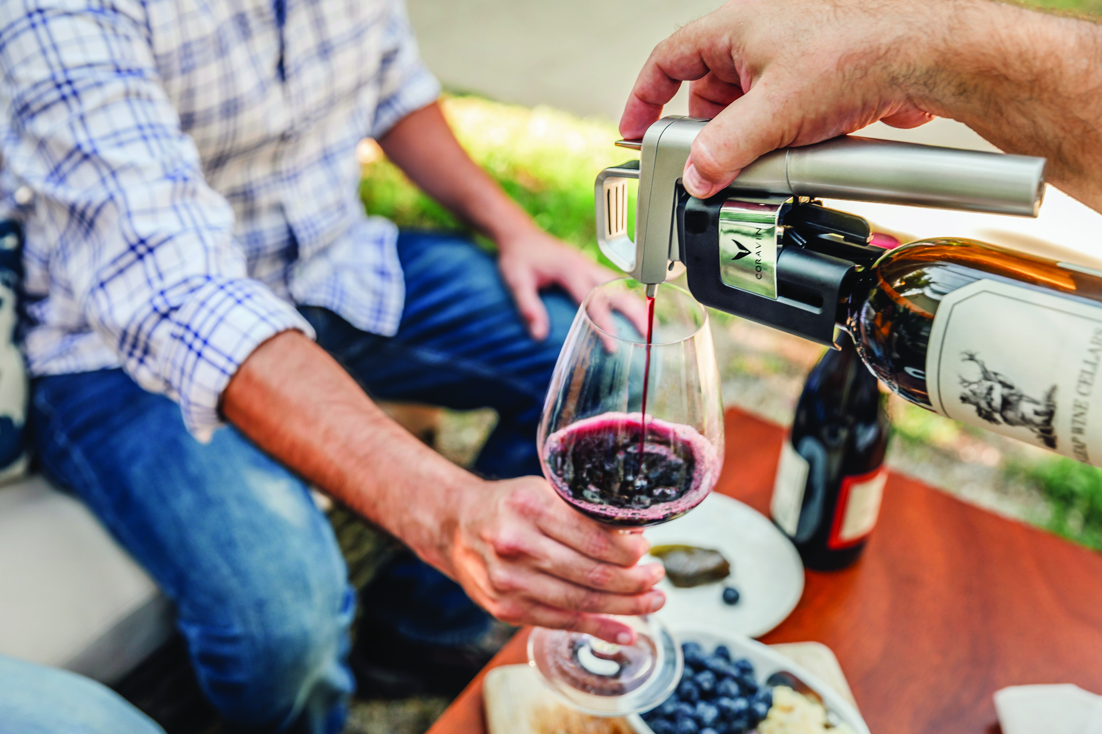 A man holding a wine glass while wine is being poured into the glass using a Coravin.