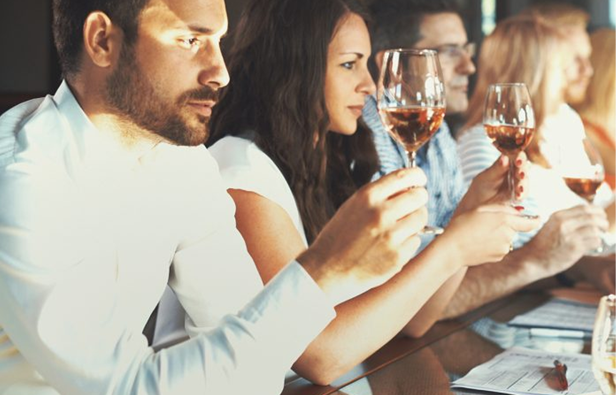 Plusieurs personnes qui participent à une dégustation de vin et chacune d’entre elles est en train de regarder dans un verre de vin.