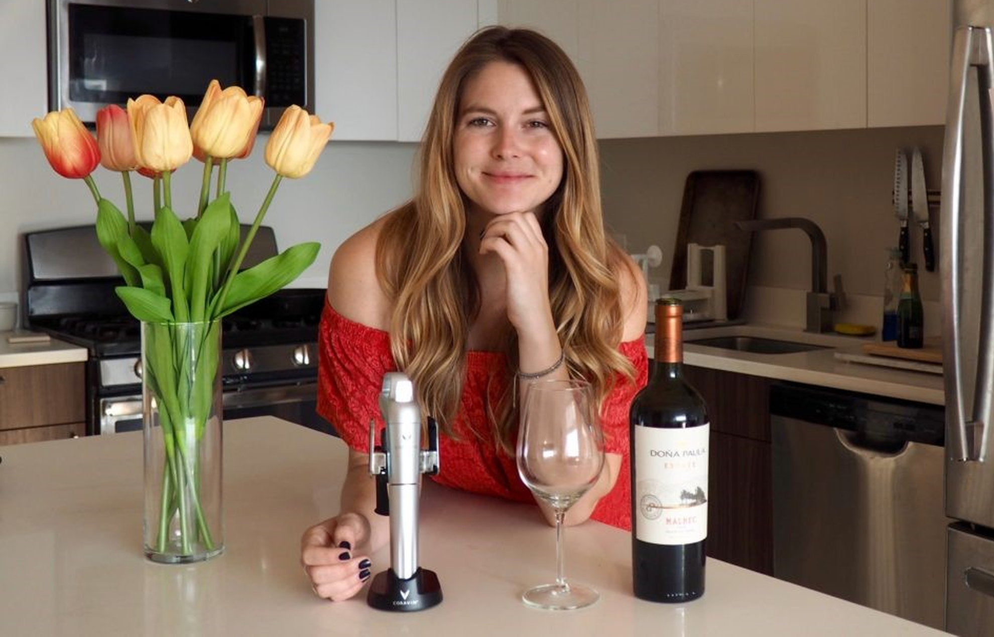 Chelsie Petras of Chel Loves Wine with a wine glass, wine bottle, and Coravin on table.