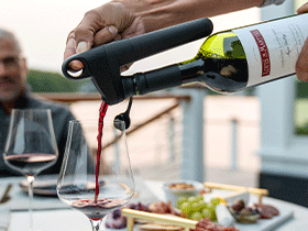Pivot System in black pouring red wine into a glass, as a man sitting at a dining table looks on.