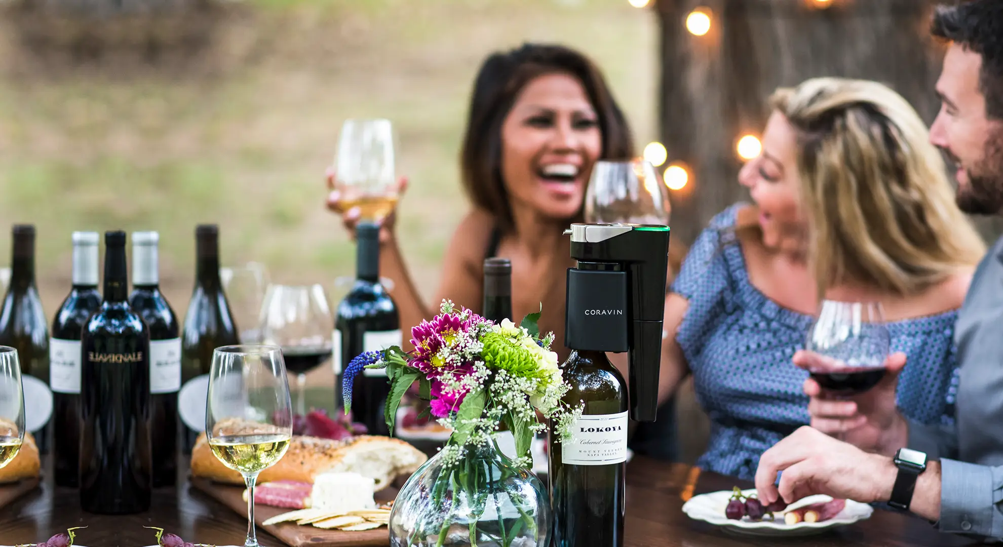 Friends using a Coravin to drink red and white wine outdoors at a picnic table.