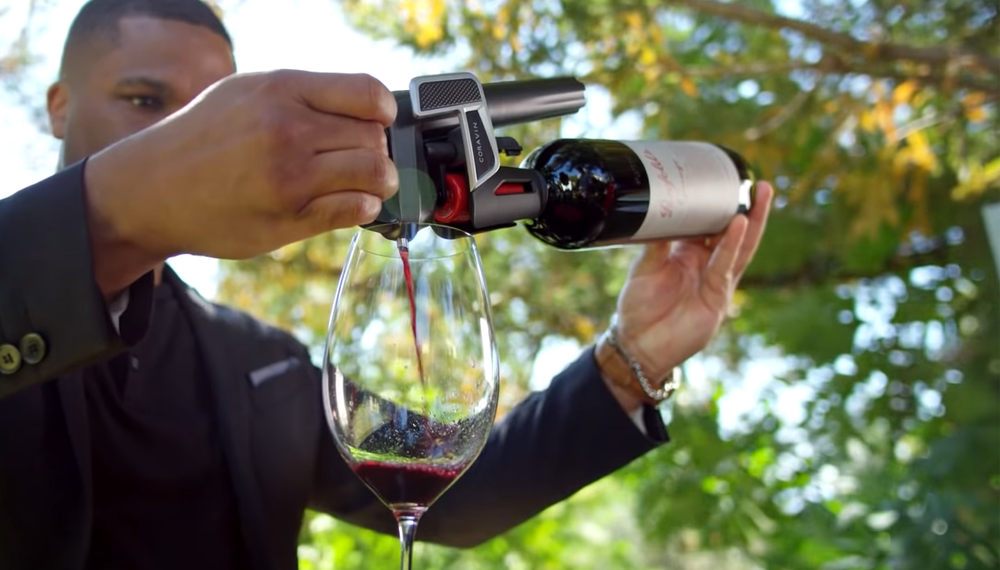 Uomo che versa vino rosso in un bicchiere mediante un sistema di conservazione del vino Coravin.
