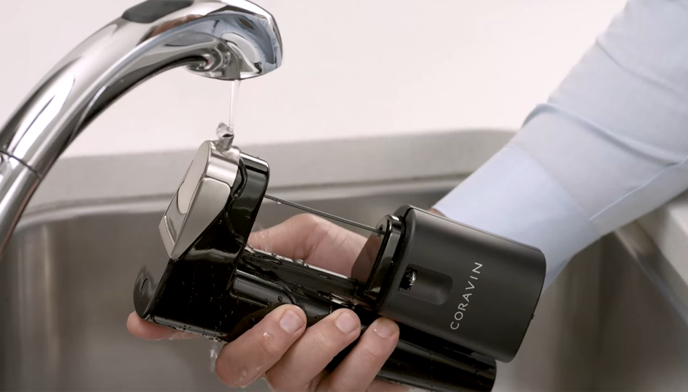 A person holding the Coravin Model Eleven under a sink faucet.