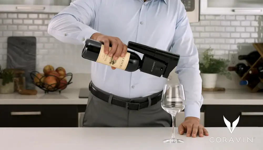 Uomo che versa vino in un bicchiere mediante un sistema di conservazione del vino Coravin Model Eleven per la mescita automatica.
