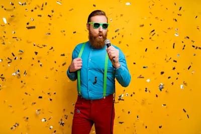 Hombre con anteojos verdes canta con micrófono bajo una lluvia de papel picado