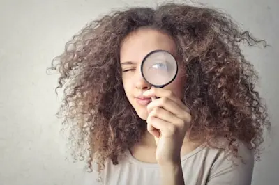 Mujer de pelo rizado mira por una lupa para analizar la baja de tasas