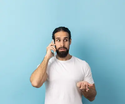 Hombre preocupado habla por teléfono con gesto de duda sobre fondo celeste