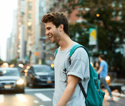 Chico joven sonriente con mochila puesta cruzando la calle caminando