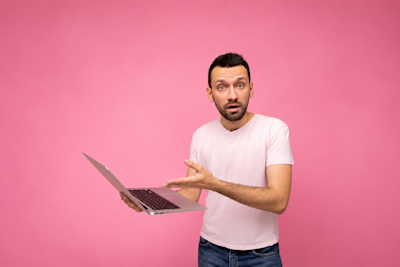 Hombre sorprendido con una notebook en la mano sobre fondo rosa
